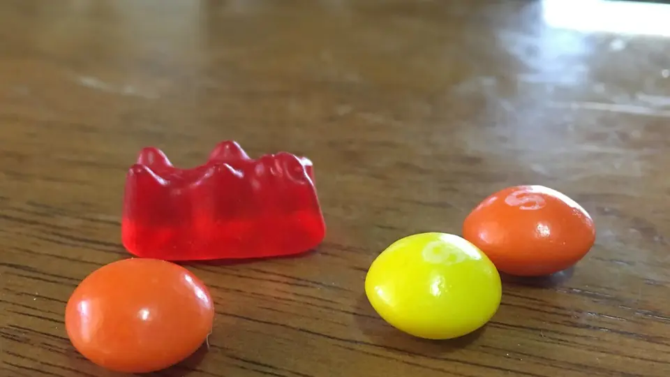 Rode gomsnoep naast drie kauwsnoepjes op een houten plank